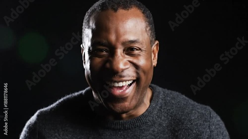 Cheerful African American man laughs heartily while looking at the camera against a black background
