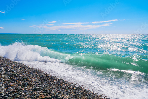 Waves on the seashore on a hot summer day. A pebble beach against the backdrop of the sea and blue sky.