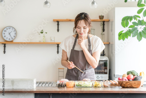 Konstfotografi A young Asian woman cooking in the kitchen (worried, confused, thinking, choosin