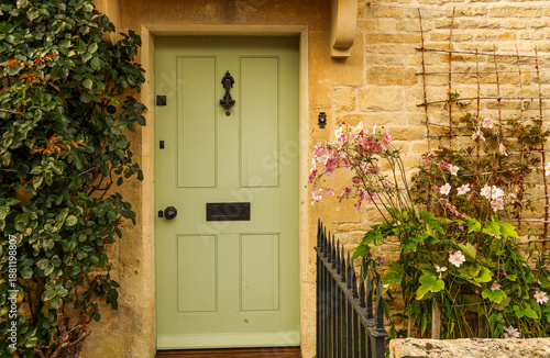 Green front door on a classic stone cottage facade with blooming anemone flowers and climbing plants