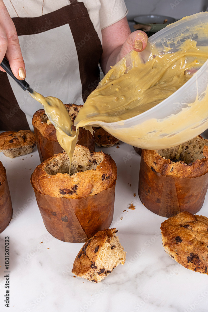 Fototapeta premium A confectioner filling several panettones with pistachio cream_vertical.