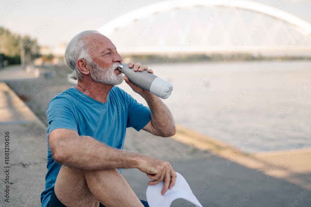 Obraz premium Senior athlete drinking water by river after exercising