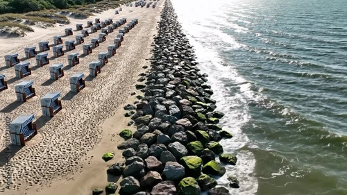 Aerial view of beach with striped chairs and stone barrier meeting the ocean under a bright sun