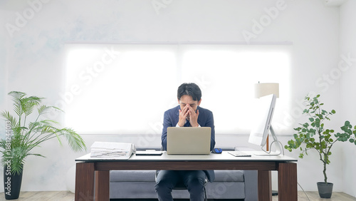 オフィスでPCを使って作業しながら悩む男性ビジネスパーソン