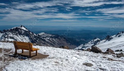 Wooden resting seat offers panoramic view across snow covered mountain peaks under bright sky