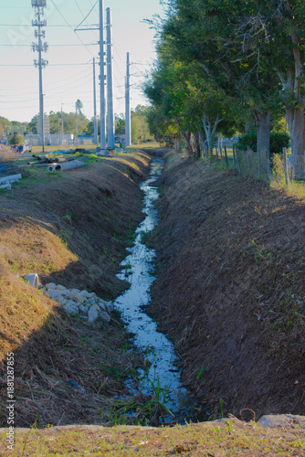 Cuadro en lienzo Rural Drainage Ditch With Water Channel, Power Lines, And Lined Trees Along Utility Corridor