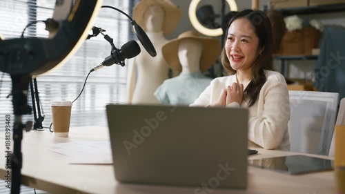  enthusiastic Asian fashion boutique owner manages her thriving online clothing store from her well-equipped home office, engaging with viewers during a live sales session on social platforms