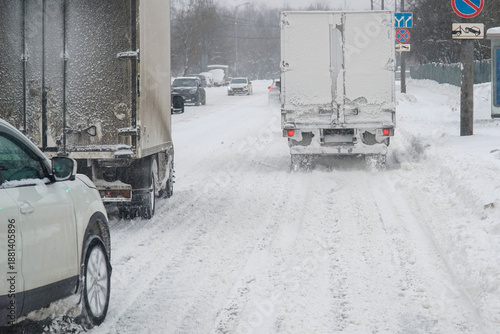 Cars drive on a snow-covered road during a snowfall.