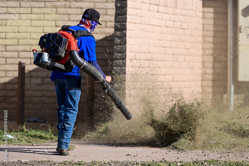 Foto Worker using a backpack leaf blower to clear weeds along a brick wall, represent