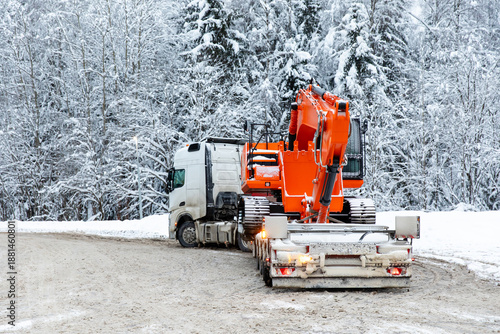 Rear view tow truck with excavator parked in winter on snowy trees background. Heavy equipment large tracked vehicle and industrial concept. High quality photo