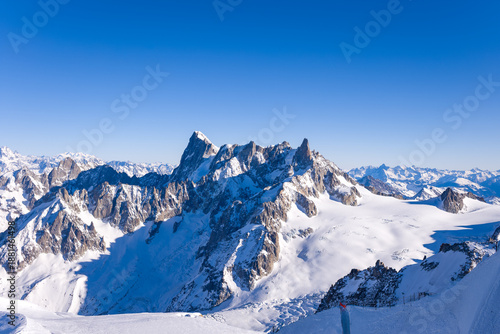 Jagged snow-covered peaks of the Grandes Jorasses rise above the expansive Glacier du Geant under a vivid blue sky, creating a dramatic alpine landscape in the Mont Blanc massif.