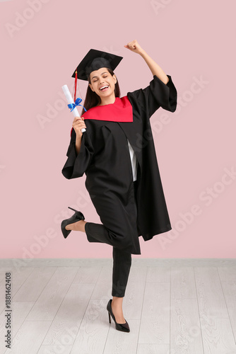 Happy female graduate with diploma near pink wall
