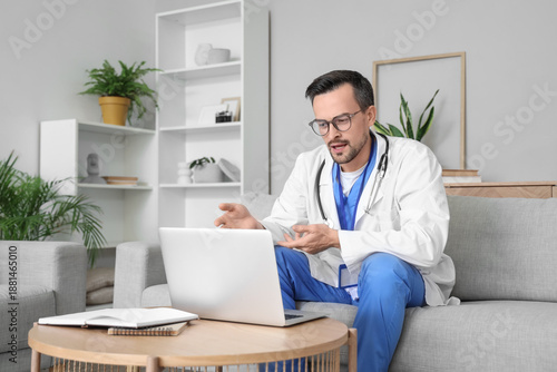Handsome doctor video chatting with patient on laptop at home