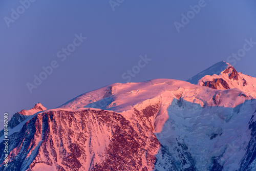 Soft pink and purple dawn light bathes the snow-covered peaks and glacier slopes of Mont Blanc, highlighting rugged textures beneath a clear sky in the French Alps.