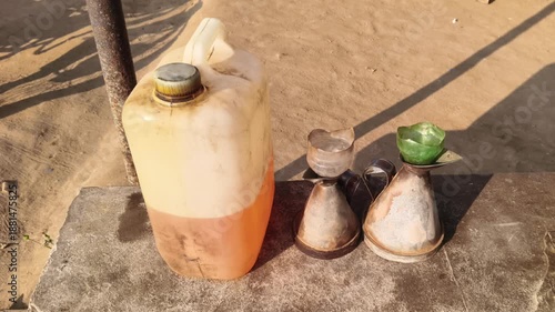 Old plastic fuel canister with traditional metal oil measuring cans on a stone bench in rural India