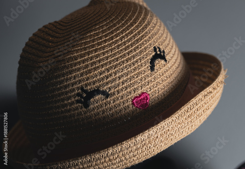 A close-up of a woven straw hat featuring subtle embroidered symbols. Soft directional light highlights texture and craftsmanship, creating a calm, minimalist mood with natural tones and gentle shadow