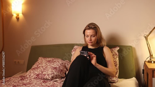 Young woman relaxing at home while using smartphone in cozy bedroom
