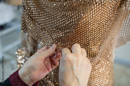 A tailor is sewing an evening gown from special gold-colored fabric embellished with stones. (stock photo)