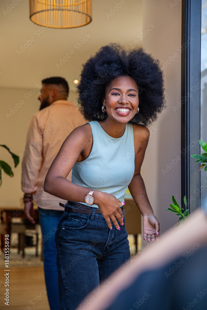 Fototapeta premium Smiling couple leaning through open doorway at modern entryway with rattan lamp and plants