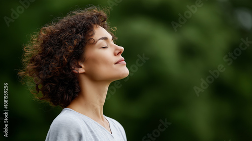 Young woman with curly hair finding peace and serenity, breathing fresh air deeply with eyes closed, enjoying nature and mindfulness in a tranquil outdoor setting, copy space