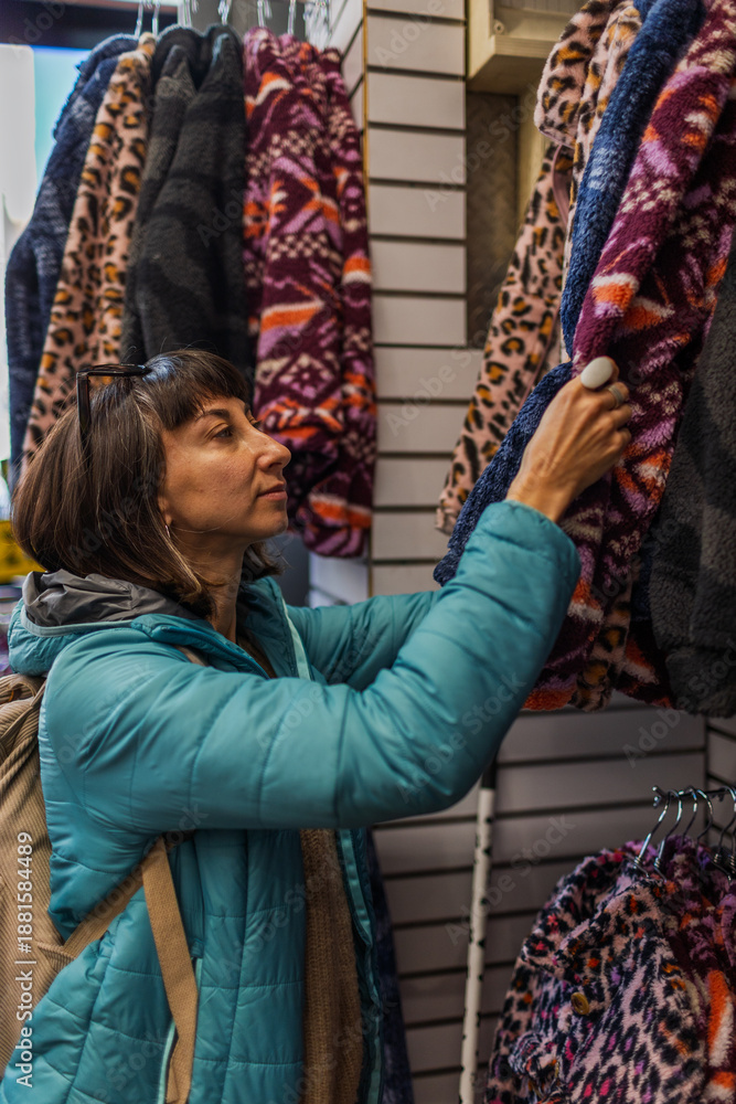 Fototapeta premium A girl examines and purchases clothes at a street market in Israel. A girl chooses a warm sweater in a store.
