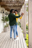 African american couple holding hands, dancing on wooden deck under pergola with lantern sconces