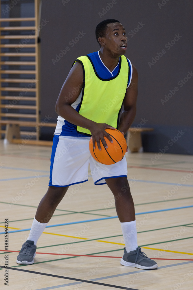 Obraz premium Athlete is holding orange basketball at waist on polished gym court, preparing to pass