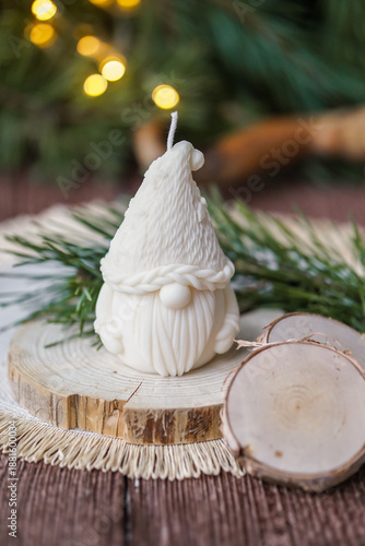 Handmade soy wax candle, standing on a wooden surface with warm festive lights and a blurred Christmas tree in the background.