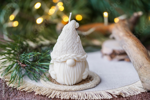 Handmade soy wax candle, standing on a wooden surface with warm festive lights and a blurred Christmas tree in the background.
