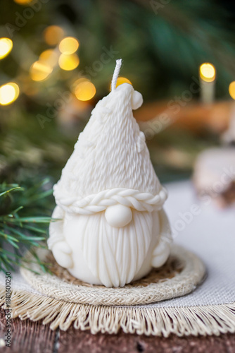 Handmade soy wax candle, standing on a wooden surface with warm festive lights and a blurred Christmas tree in the background.