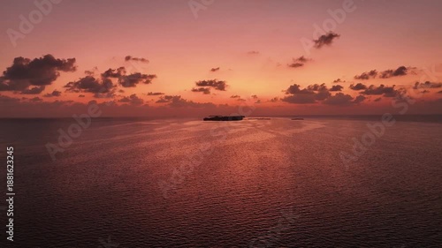 Aerial view of the tranquil ocean reflecting the vibrant hues of the sunset and distant islands, creating a serene landscape, Goidhoo, Baa Atoll, Maldives.