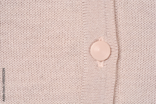 A detailed shot of a beige wool knitted cardigan featuring a plain round button on the front opening