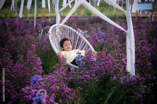 A little child boy sitting and sleeping on a chair in the flower garden. An Asian boy kid is taking a nap with purple flowers.