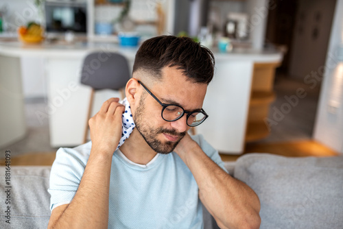 Tableau sur toile Young man sitting on a sofa and using an ice pack for neck pain and cervical spi
