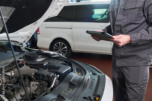 Canvas Print Unrecognizable man inspecting car engine while holding digital tablet in auto re