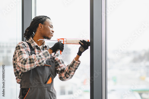 Cuadro en lienzo African American Construction worker applying silicone sealant to window frame