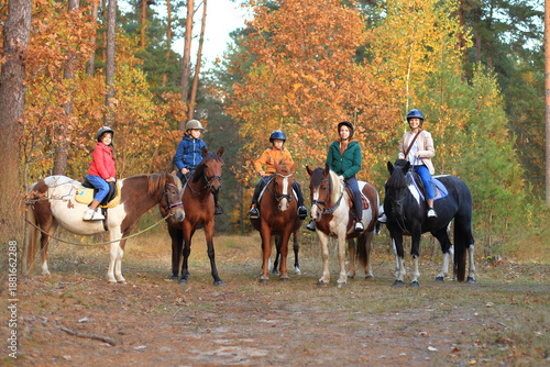 A group of five riders, including children and an adult, pose on their horses in a vibrant autumn forest, showcasing a joyful outdoor equestrian experience.