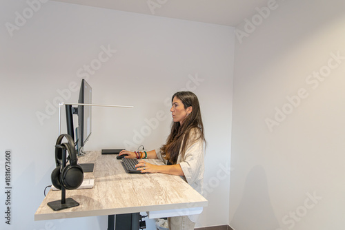 Fotografija Woman standing working at a modern height adjustable desk with computer and head