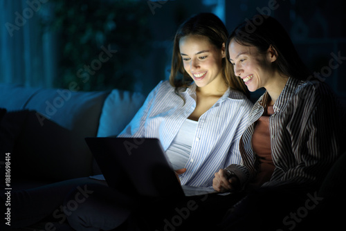 Two happy friends watching media online on laptop in the night