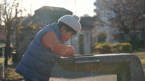 Japanese child quenching thirst at a public water fountain on a sunny day in the park