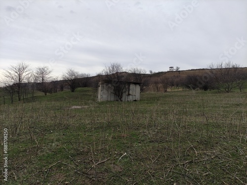 Abandoned concrete building on a grassy autumn field with bare trees and cloudy sky