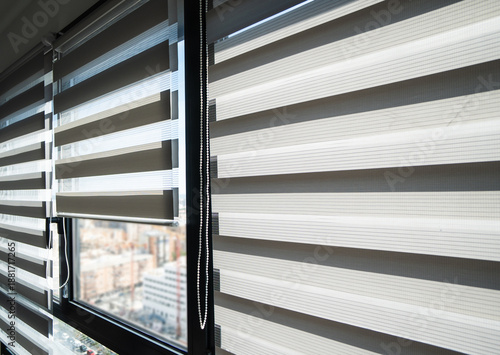 Fotografie Zebra roller blinds covering apartment window with soft city background, modern