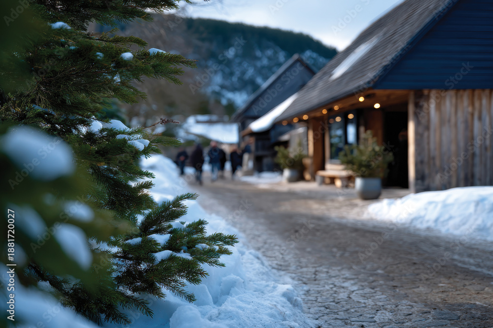 Fototapeta premium A picturesque village street blanketed in snow showcases rustic wooden buildings and evergreen trees, evoking warmth and charm amid a winter wonderland setting.