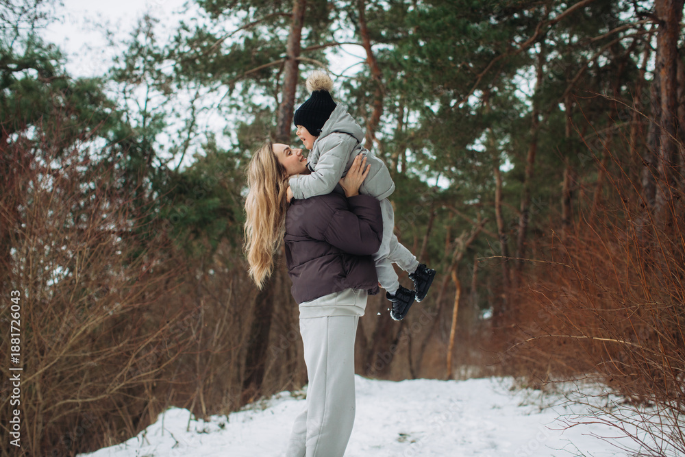 Obraz premium Mother lifting young child playing in winter forest