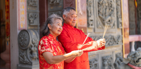 Asian senior couple in red traditional outfits giving chinese new year greeting at temple, showing respect and cultural pride, celebrating festival with warm gesture, Lunar New Year 2026 festival