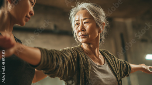 Black personal trainer helping an elderly Japanese client improve balance and stability in a wellness studio. Senior asian woman doing exercises for better health. Healthy lifestyle.