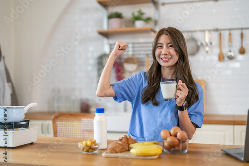 Obraz na plátně Strong asian nurse wearing blue scrubs flexing arm while holding glass of milk i