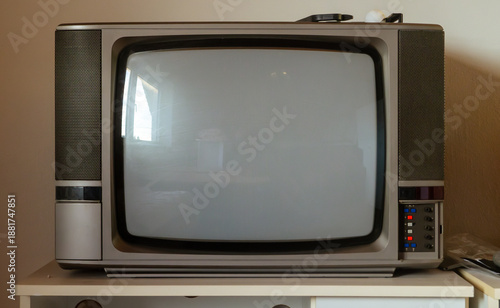 An old TV set stands on the table, turned off. An old, heavy TV set with a gray screen and light coming from the window