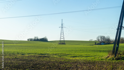 A high-voltage power line stands in the middle of a green field on a clear sunny day