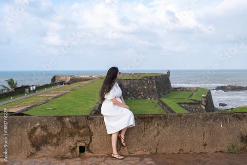 A woman in a white dress sits on the walls of Galle Fort, Sri Lanka.